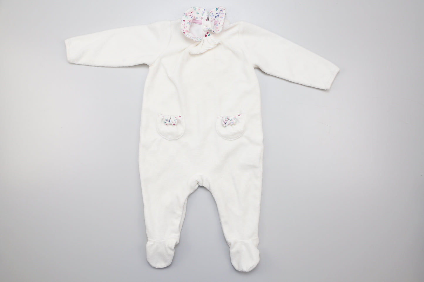 Weißer Babystrampler mit Füßchen für Mädchen, Kragen und zwei kleinen Taschen vorne. Unten mit Druckknöpfen. 74