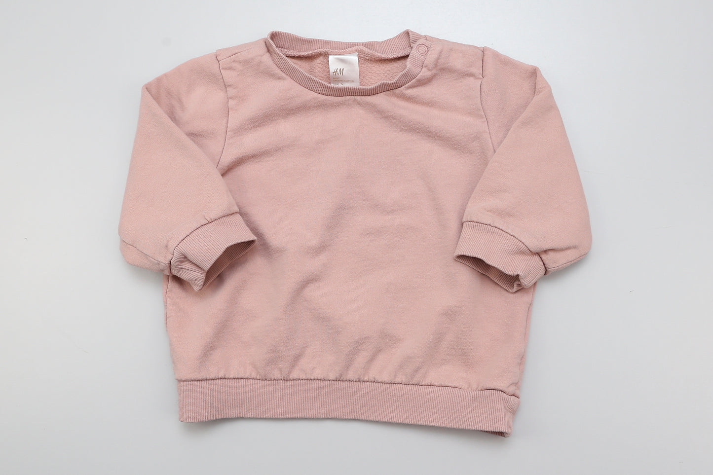 Helllachsfarbener Sweatshirt mit Druckknöpfen an der Schulter. 