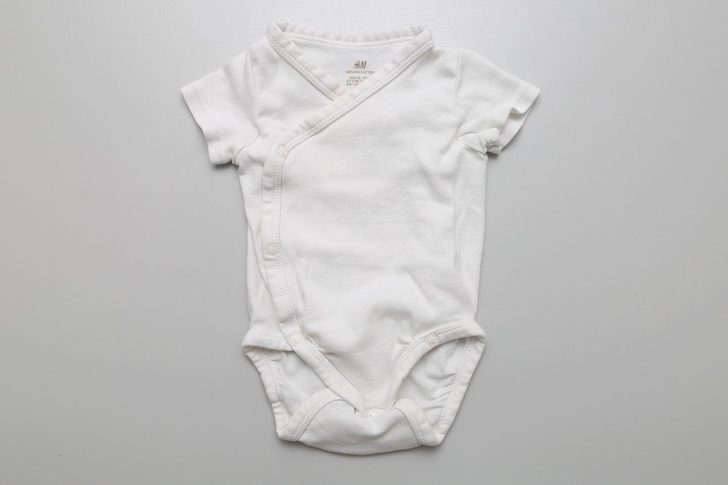 Weißer Kurzarm-Wickelbody aus Bio-Baumwolle in Größe 56. Sanft zur Babyhaut und praktisch zum Anziehen.