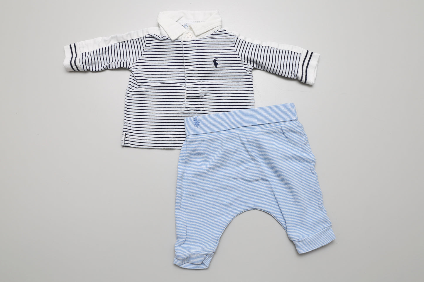 Blaues Jungenset aus Baumwolle in Größe 62. Das langärmlige Poloshirt mit Kragen hat Knöpfe vorne für einfaches Anziehen. Die Hose ist hoch geschnitten und bequem. Minimale Gebrauchsspuren an der Hose sichtbar.
