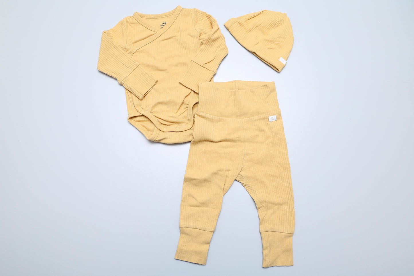 Mehrgrößiges Body-Leggings-Set mit Mütze aus Bio-Baumwolle. Die Länge des Bodys ist durch Druckknöpfe verstellbar, die Ärmel des Bodys und die Beine der Leggings können umgeschlagen werden. Das Set besteht aus dehnbarem, geripptem Material.