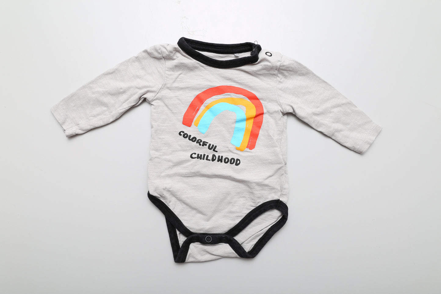 Grauer Langarm-Body aus Baumwolle mit Regenbogen-Motiv, an der Schulter mit Druckknöpfen. Größe 56.