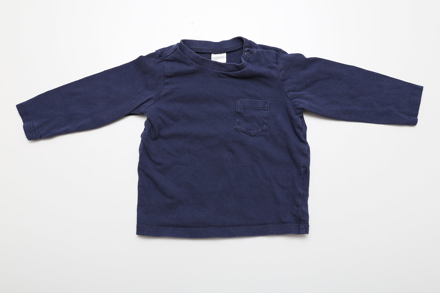 Dunkelblaues Langarmshirt, Größe 74. Aus 100 % Baumwolle, an der Schulter mit Druckknöpfen. Der Stoff ist entlang der Nähte (z. B. an der Tasche) leicht abgenutzt.