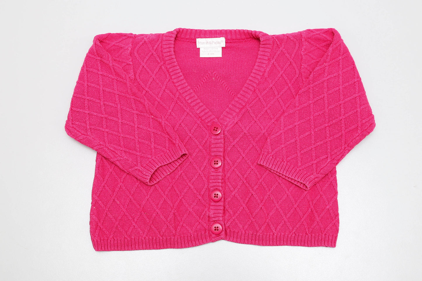 Pinker Strickcardigan in Größe 68, vorne mit Knöpfen. Bügelspuren sind leicht sichtbar.
