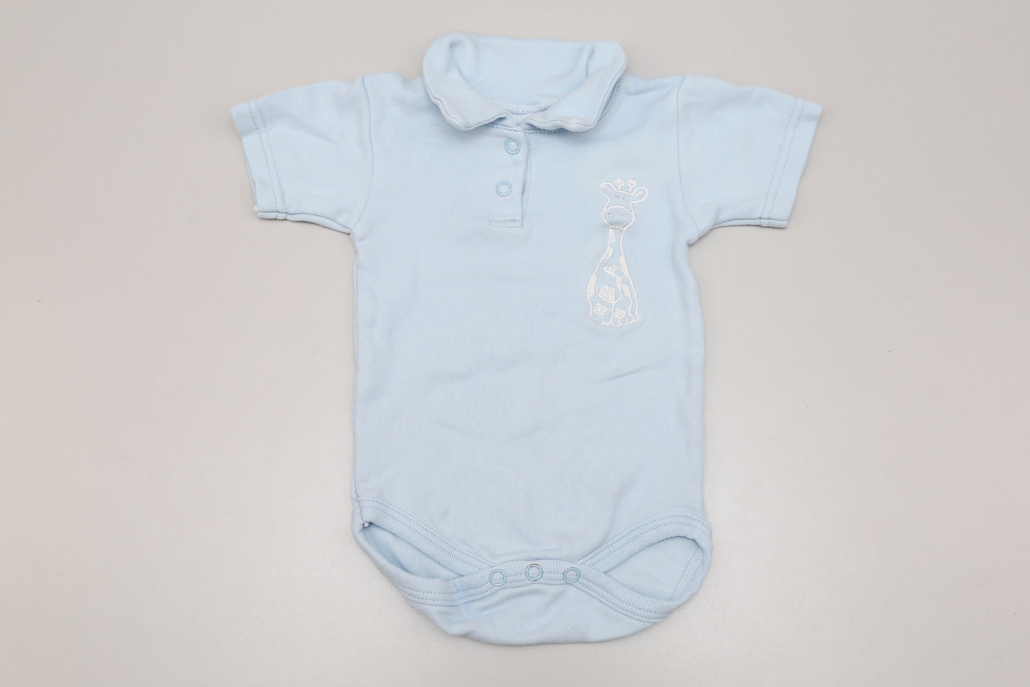 Hellblauer Giraffen-Polo-Body mit Kurzarm, vorne mit zwei Druckknöpfen. Für 6 Monate alte Babys, entspricht der Größe 68-74.