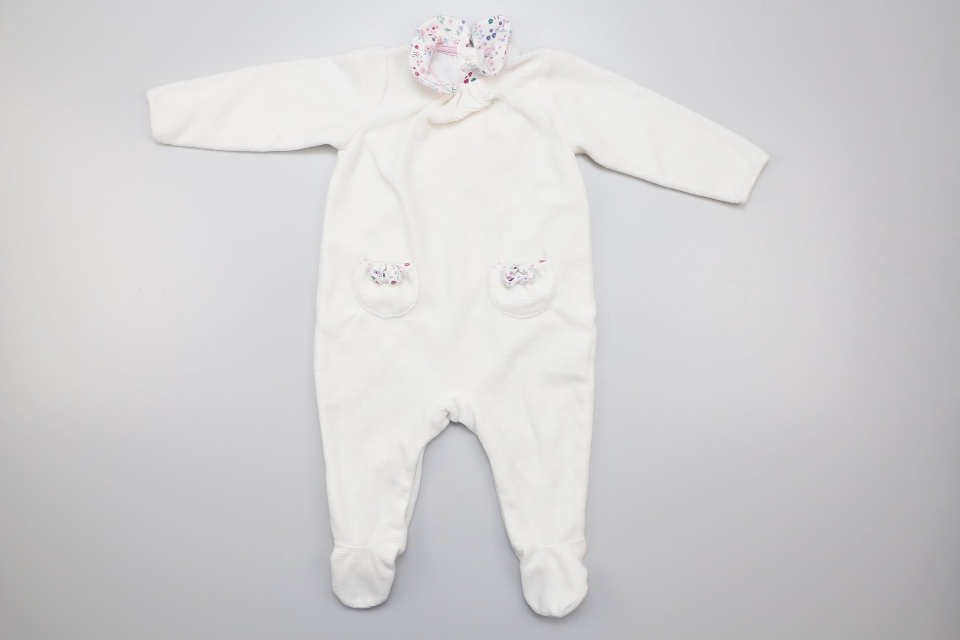 Weißer Babystrampler mit Füßchen für Mädchen, Kragen und zwei kleinen Taschen vorne. Unten mit Druckknöpfen. 74