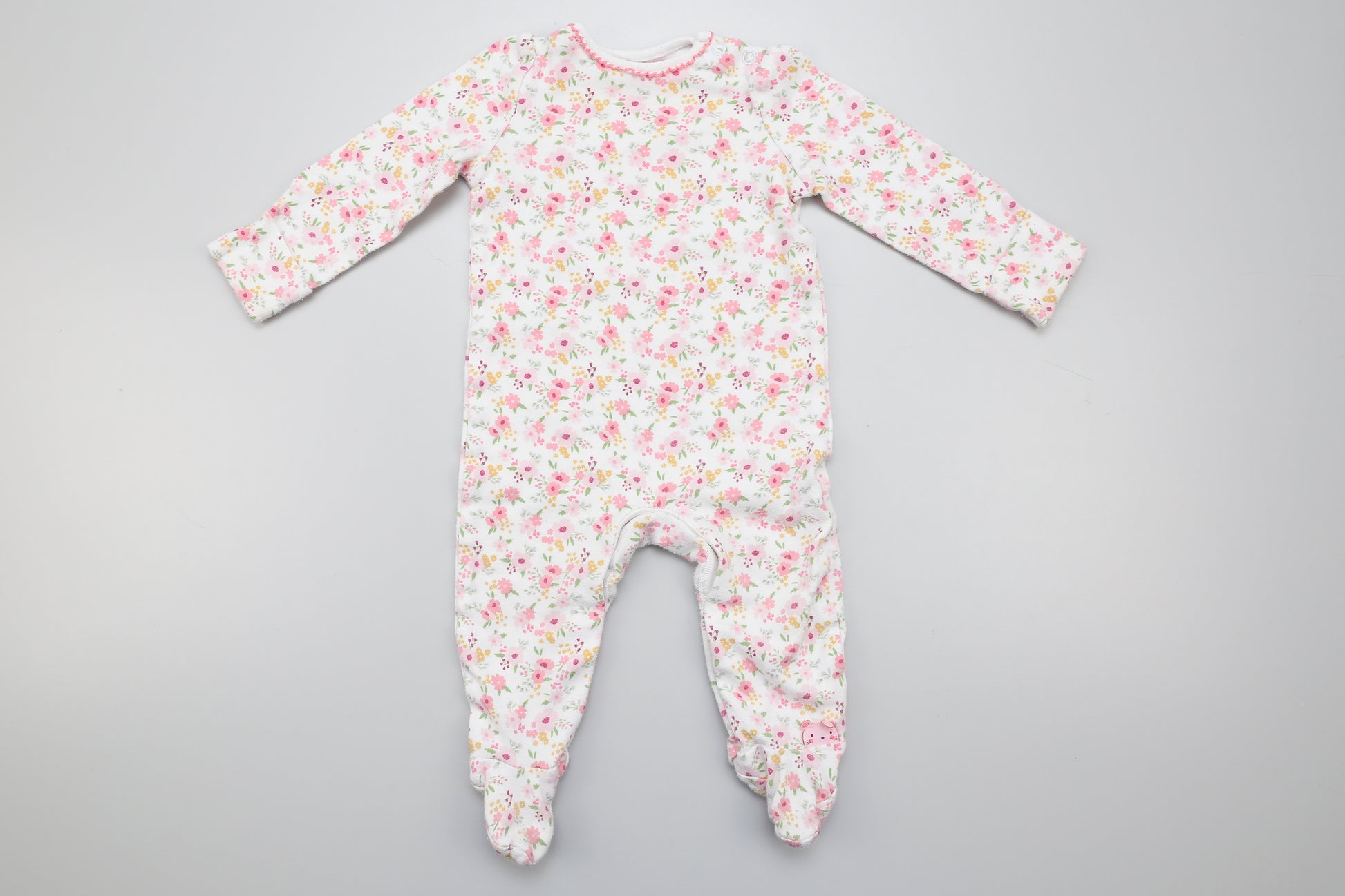 Kleine Blumen gemusterter Strampler aus Baumwolle mit umklappbaren Ärmeln. Unten mit Druckknöpfen. Zwei Druckknöpfe am Hals erleichtern das Ankleiden. 68