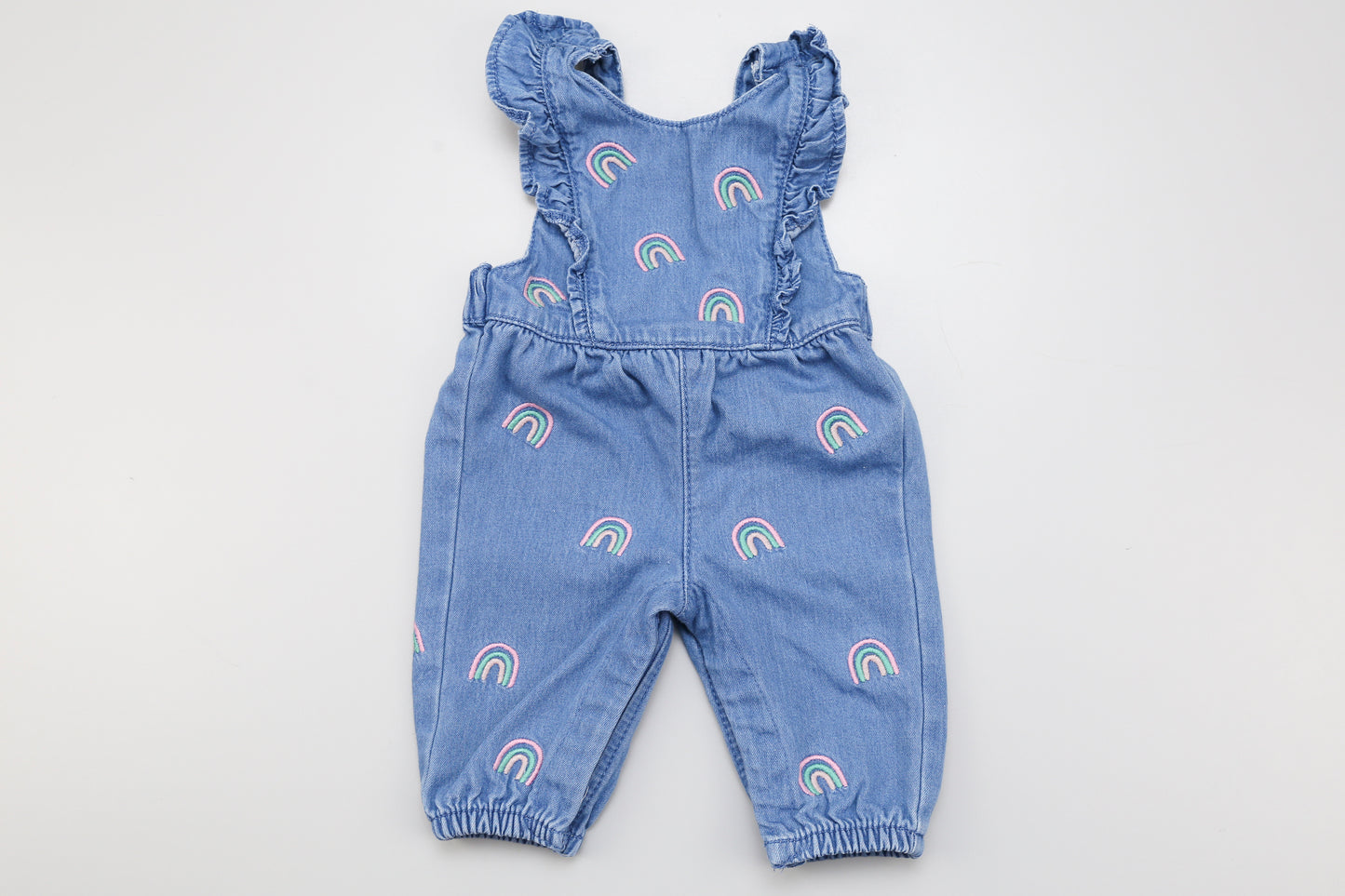 Jeans-Latzhose mit Regenbogenmuster und Rüschen vorne. Im Schritt mit Druckknöpfen und hinten abnehmbare Träger für leichteres Anziehen.