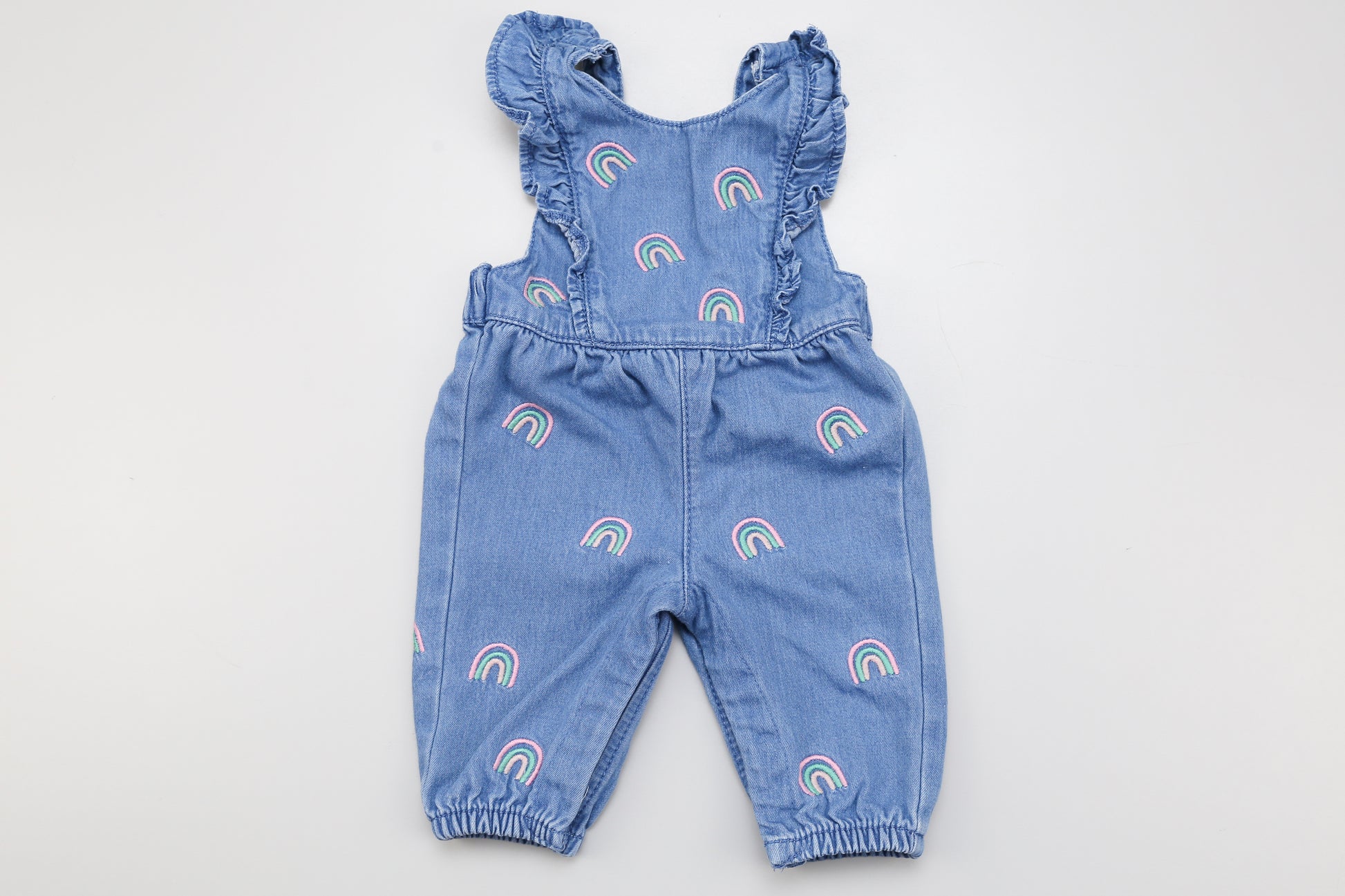 Jeans-Latzhose mit Regenbogenmuster und Rüschen vorne. Im Schritt mit Druckknöpfen und hinten abnehmbare Träger für leichteres Anziehen.