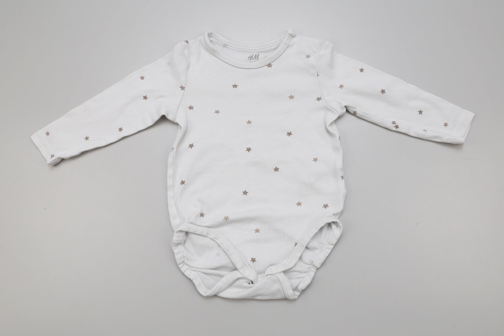 Weißer Langarm-Babybody mit kleinen Sternen und Druckknopf am Halsausschnitt, Größe 74, leicht vergraut

