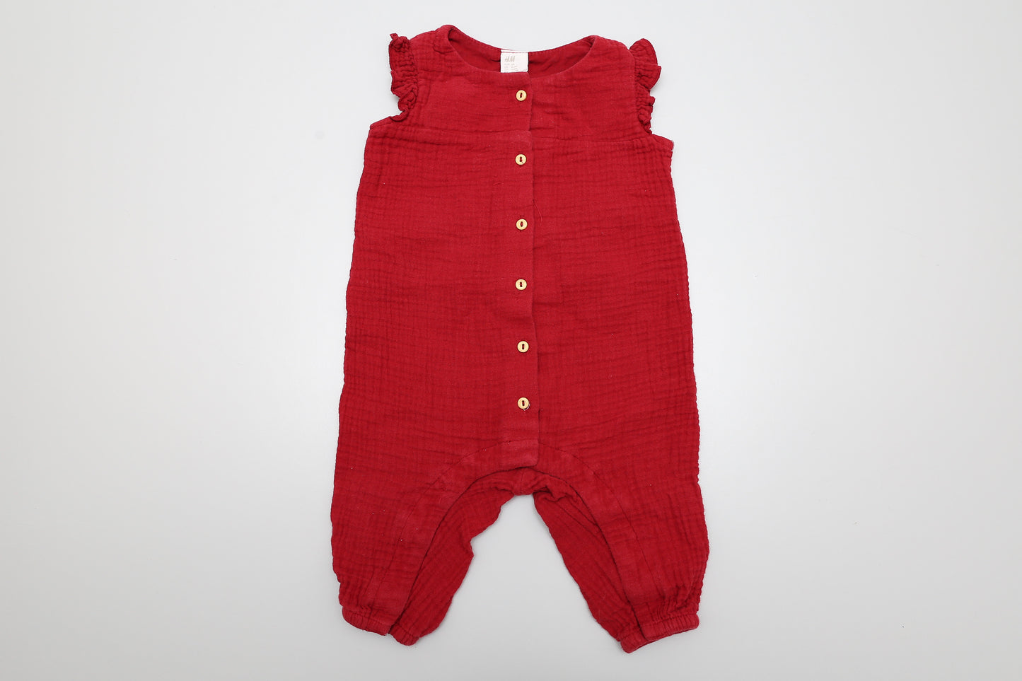 Bordeauxrote Latzhose aus Baumwolle mit Rüschen, vorne mit Knöpfen, unten mit Druckknöpfen zu öffnen. Größe 68.