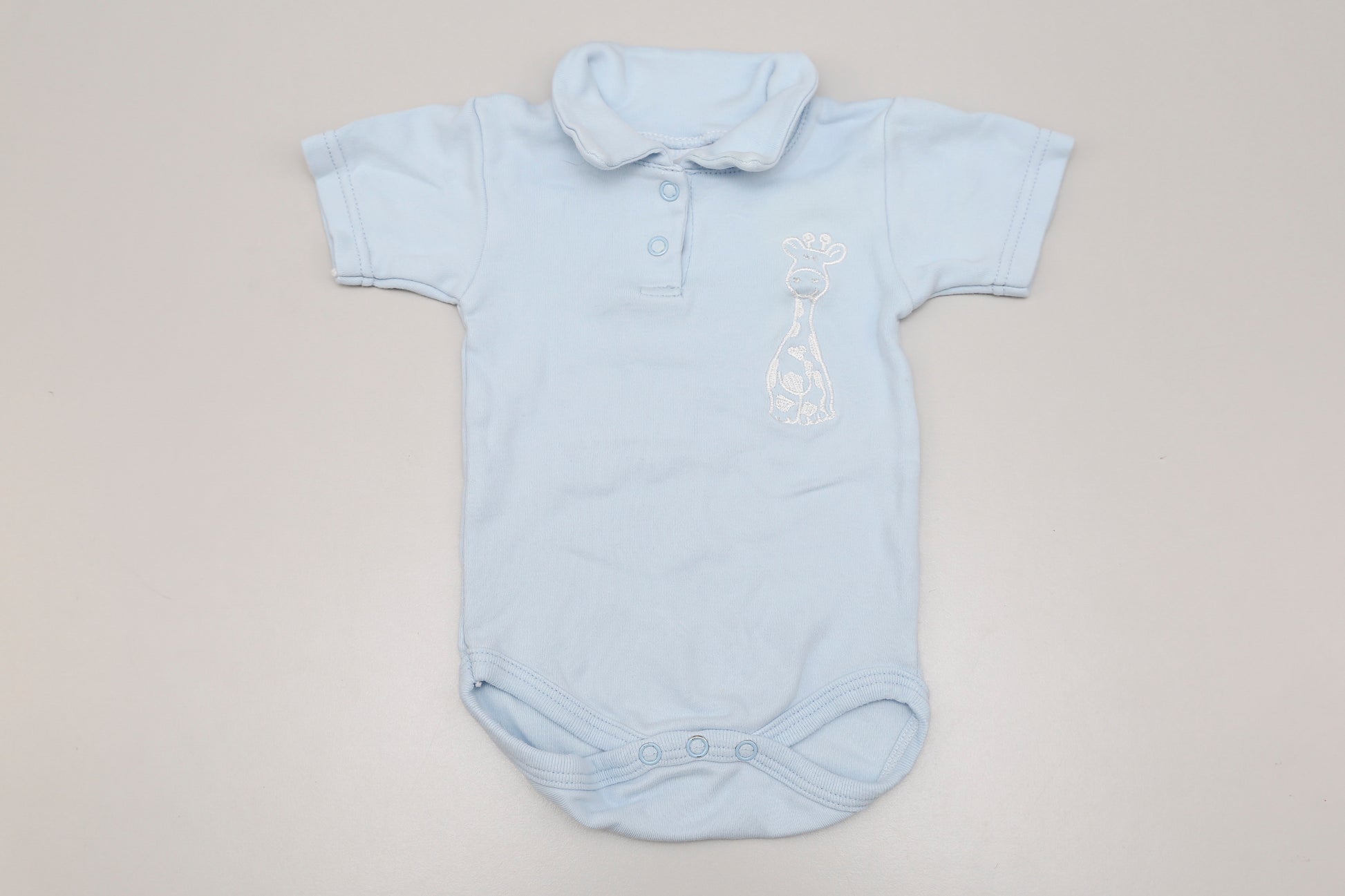 Hellblauer Giraffen-Polo-Body mit Kurzarm, vorne mit zwei Druckknöpfen. Für 6 Monate alte Babys, entspricht der Größe 68-74.